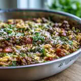 Steamy Comforting Ground Beef Orzo Dinner served in a rustic skillet, garnished with fresh parsley and a side of crusty bread.