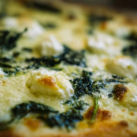 Freshly baked Spinach Ricotta Pizza sliced into wedges, served with a crisp green salad nearby.