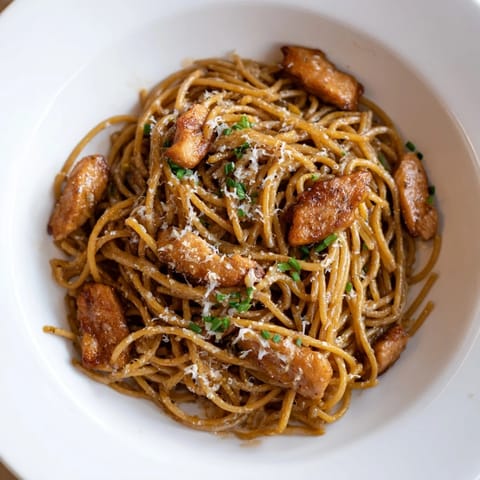 A close-up of the Brown Butter Lemon Chicken Pasta, featuring tender chicken nestled in glossy, herbed pasta with lemon wedges on the side.  