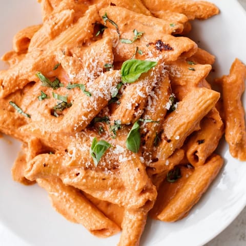 A skillet of creamy roasted red pepper pasta, garnished with fresh basil and a dusting of Parmesan cheese.  