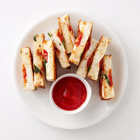 Golden, melty Caprese Grilled Cheese Dippers with fresh mozzarella, tomato, and basil, sliced and ready for dipping into warm marinara sauce.