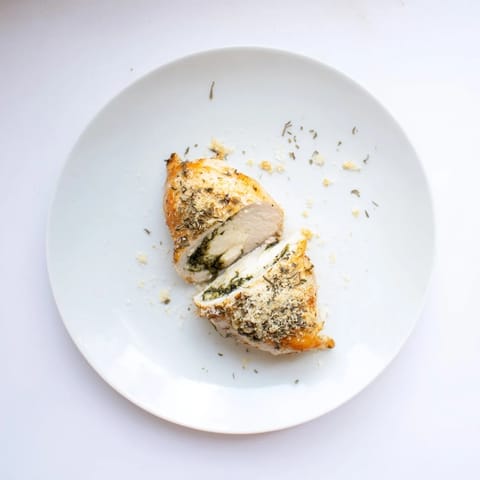 Sliced Mozzarella & Pesto Stuffed Chicken shows juicy interior and herb Parmesan crust on a dinner plate.