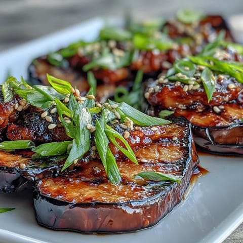Silky roasted miso glazed eggplant halves garnished with sesame seeds and green onions on a white plate.