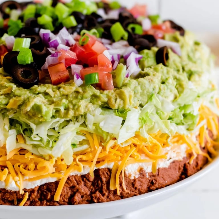 Enjoy a taste of this classic Seven-Layer Dip, featuring layers of refried beans and cheese alongside toppings.