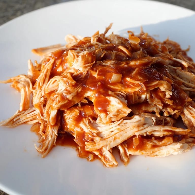 Shredded BBQ pulled chicken in a slow cooker, offering a glimpse of the tender, juicy meat inside.