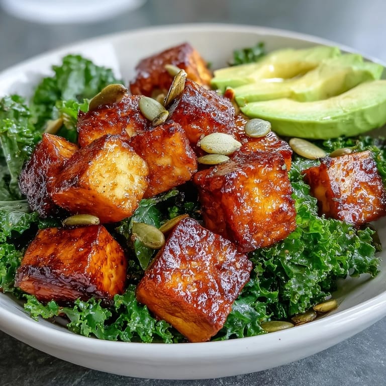 Hearty breakfast bowl featuring crispy tofu cubes, wilted kale, and ripe avocado slices served with lemon wedges and pumpkin seeds.