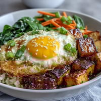 A vibrant tofu jammy egg breakfast bowl with seasoned tofu, fresh greens, and a zesty ginger scallion sauce.  