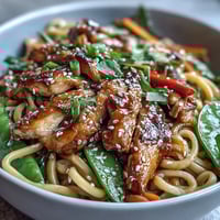 Sesame Chicken Noodle Bowl with tender chicken, crisp vegetables, and savory sesame sauce, served in a vibrant Asian-inspired dish.  